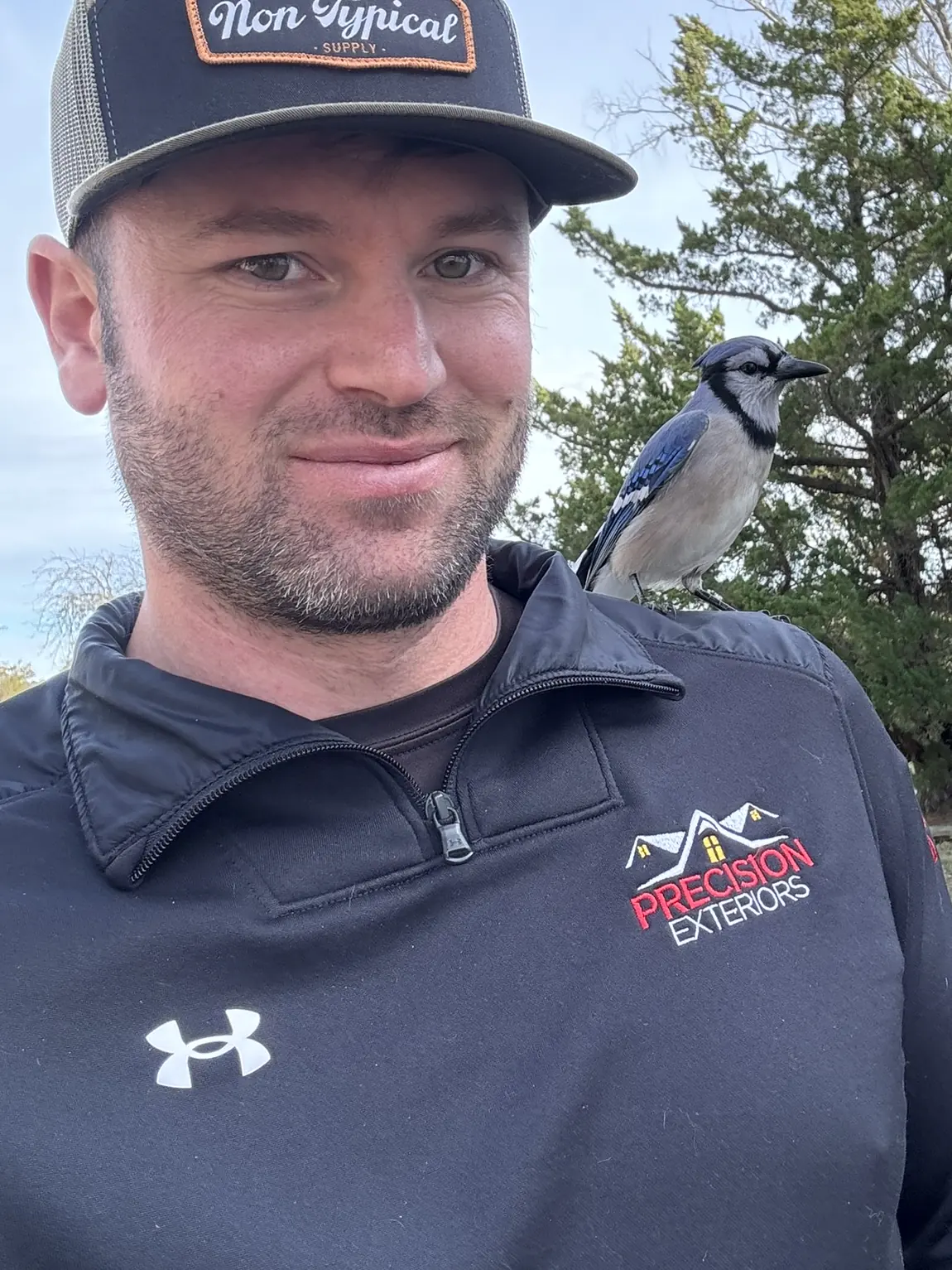 Adam Whitaker, founder of Pufferfish Media, outdoors in Precision Exteriors work gear with a blue jay perched on his shoulder